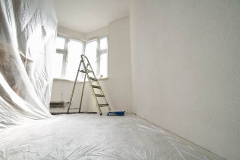 A white room with transparent painting coverings and a ladder.