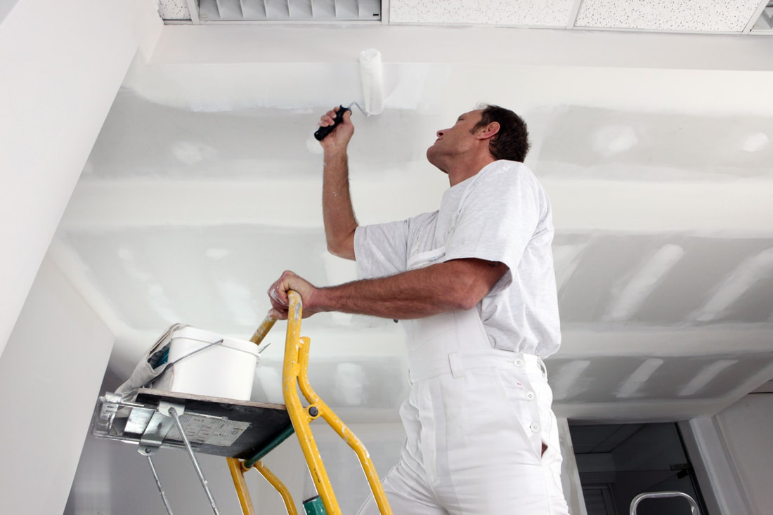 A picture of a painter on a ladder mudding ceiling in white.